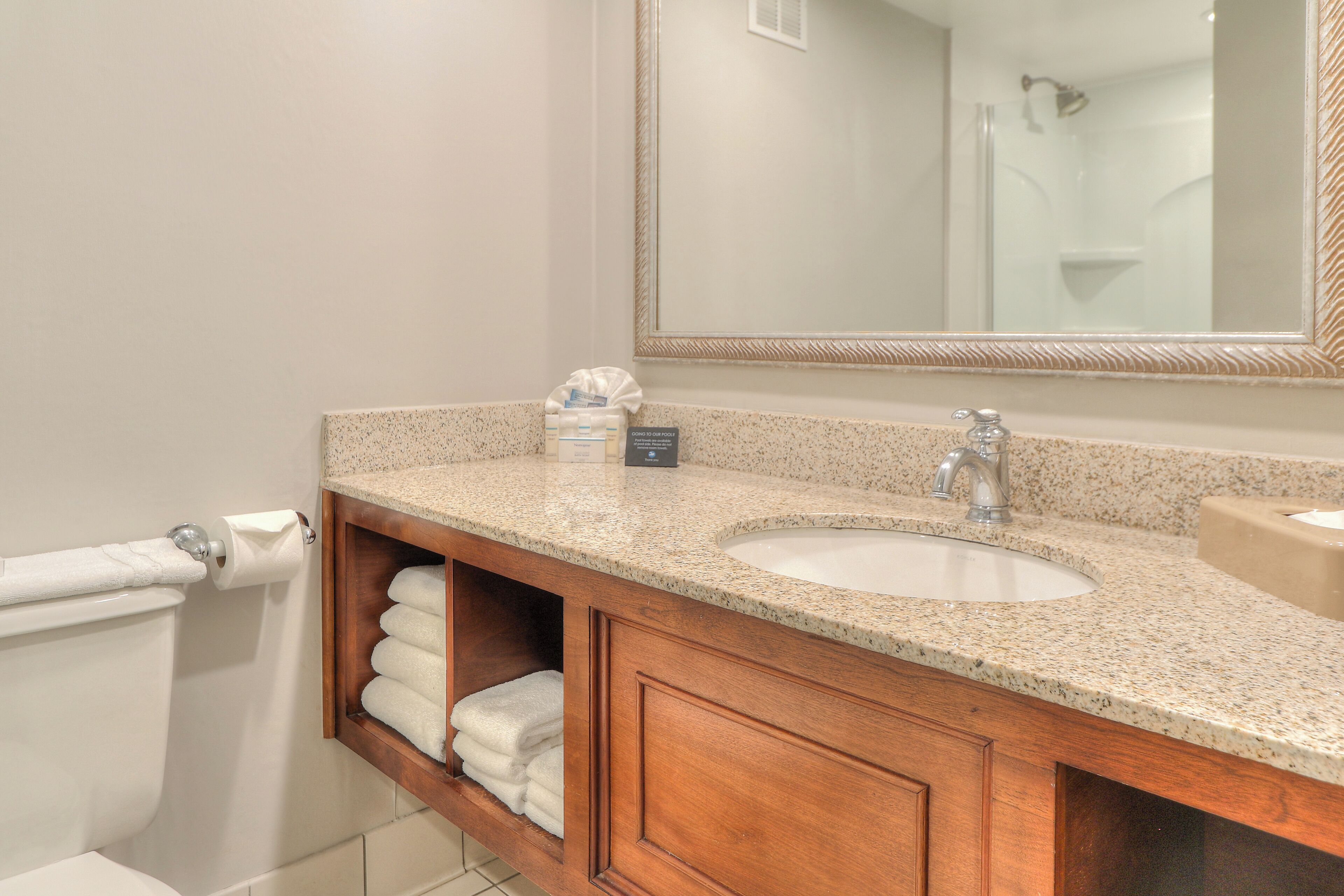 A bathroom with a granite countertop, two sinks, a mirror, and a towel rack.