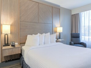 A hotel room with a large bed, two bedside tables with lamps, a chair, and a view of the outdoors through a window. - The Ramsey Hotel and Convention Center Pigeon Forge (Pigeon Forge)