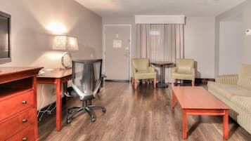 A hotel room with a wooden desk, two armchairs, a sofa, a small table, and a lamp.