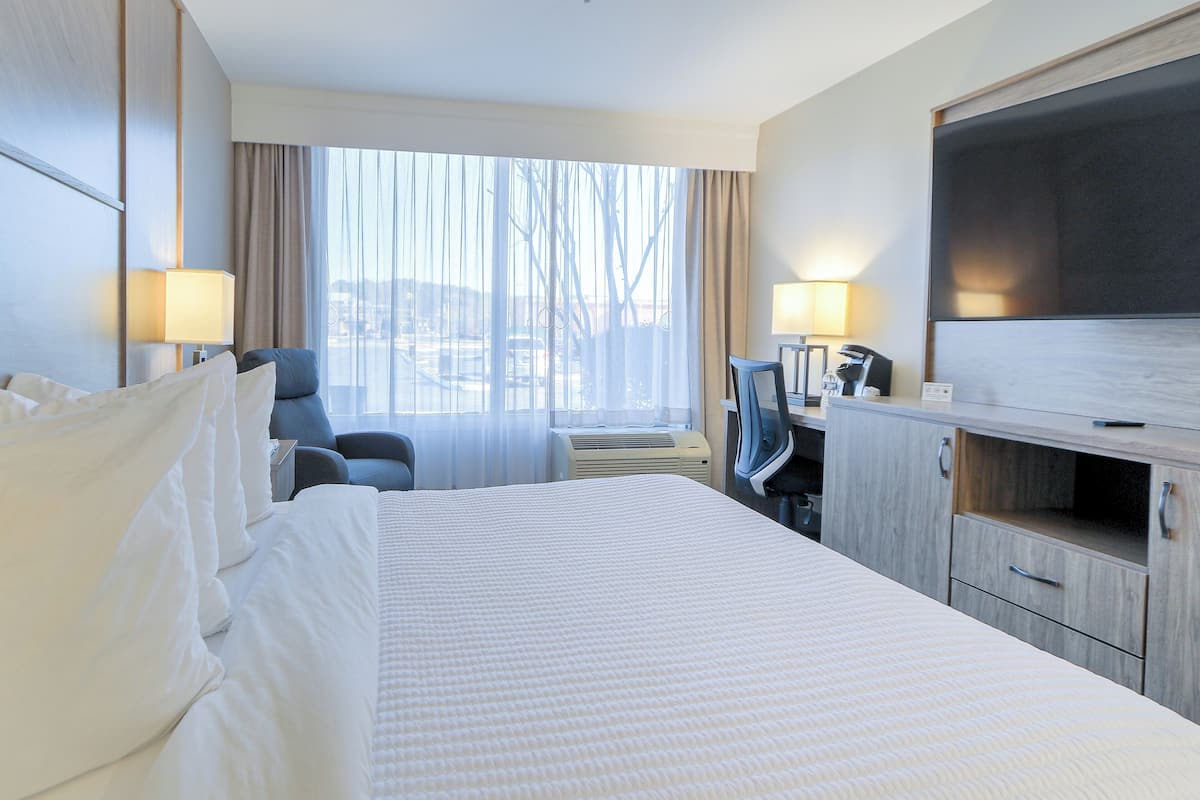 Habitación de hotel con una cama grande, un escritorio con computadora, un televisor y una ventana con cortinas.