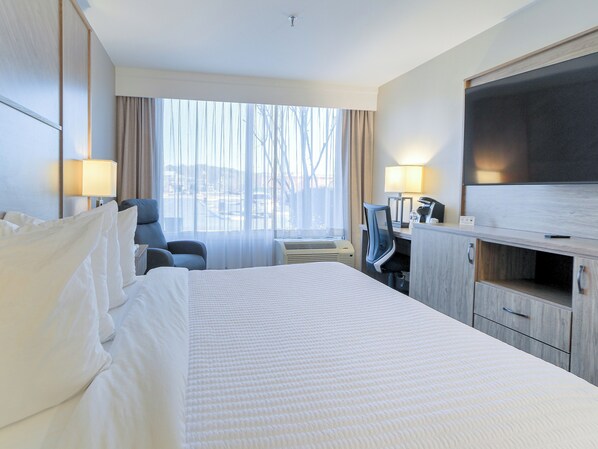 A hotel room with a large bed, a desk with a computer, a TV, and a window with curtains.