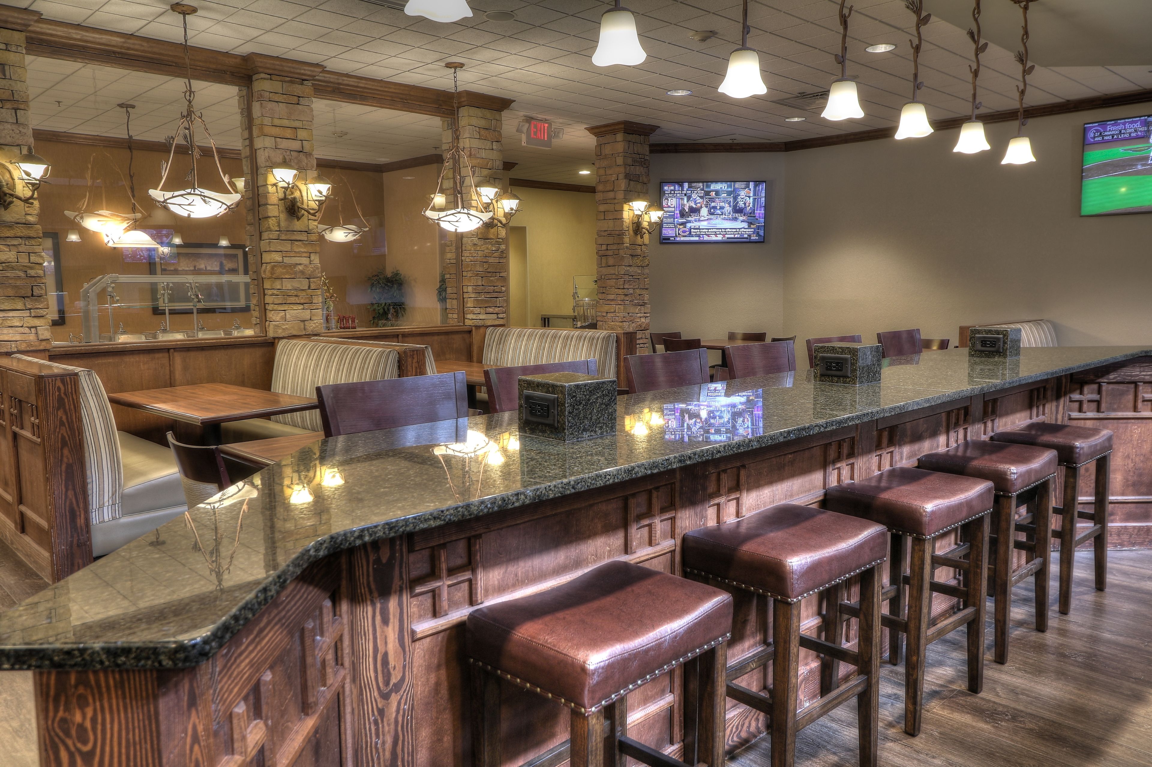 A bar area with a long counter, multiple stools, and hanging lights.