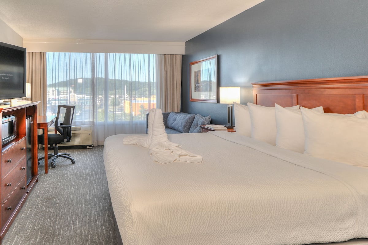 Habitación de hotel con una cama grande, un escritorio con silla, televisión y ventana con cortinas.