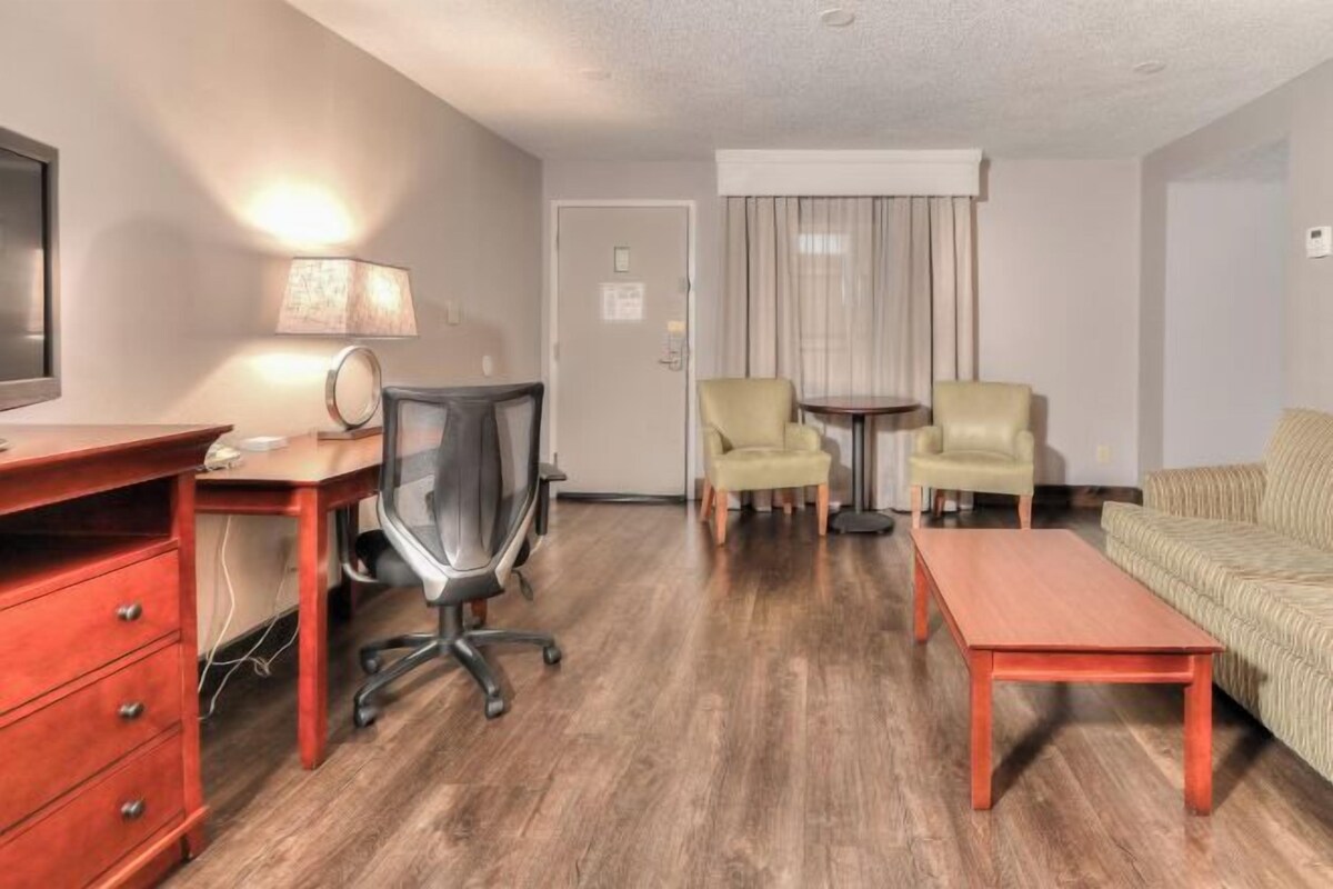 A hotel room with a wooden desk, two armchairs, a sofa, a TV, and a lamp.