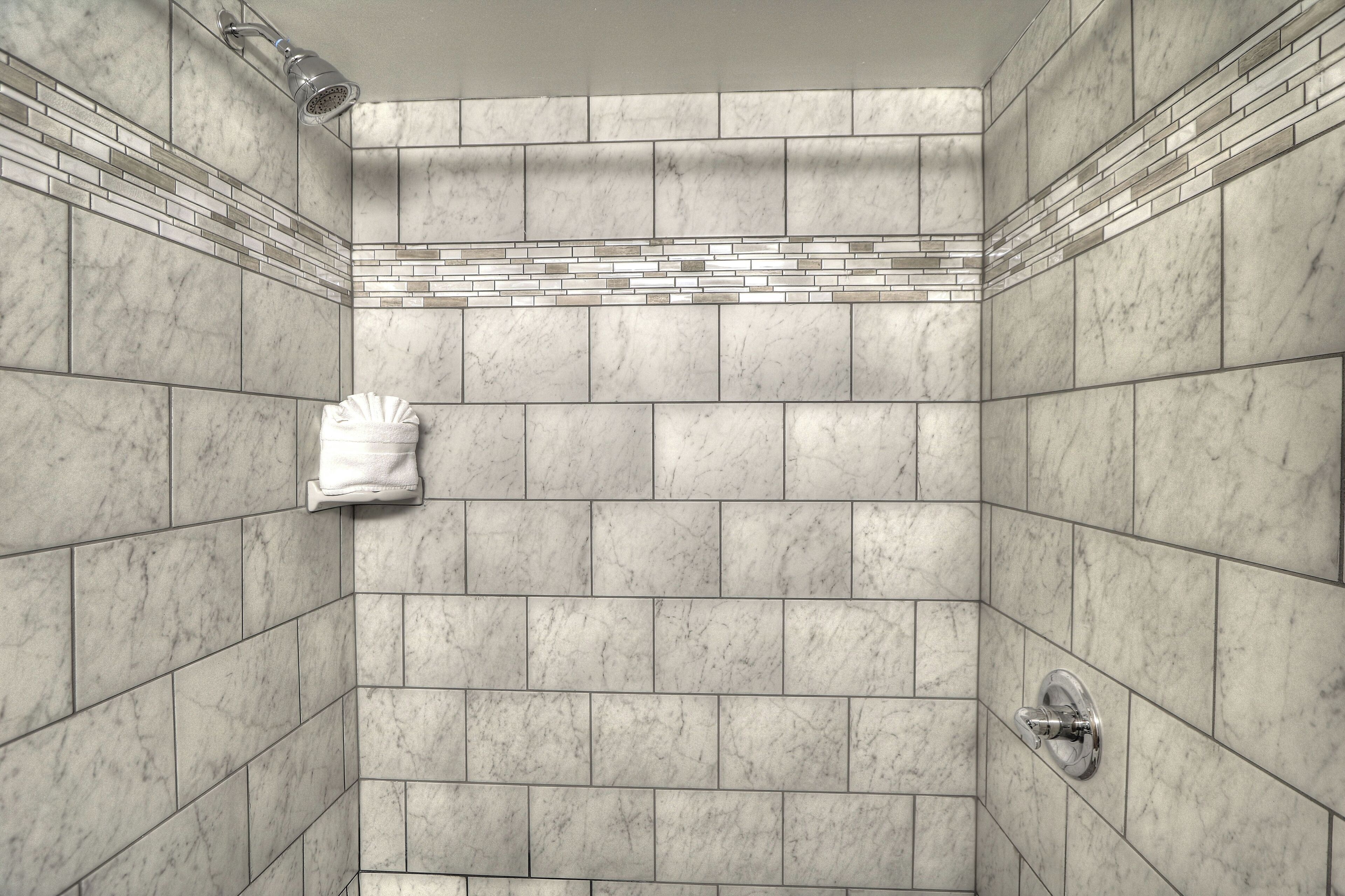 A shower with a tiled wall, a towel rack, and a showerhead.