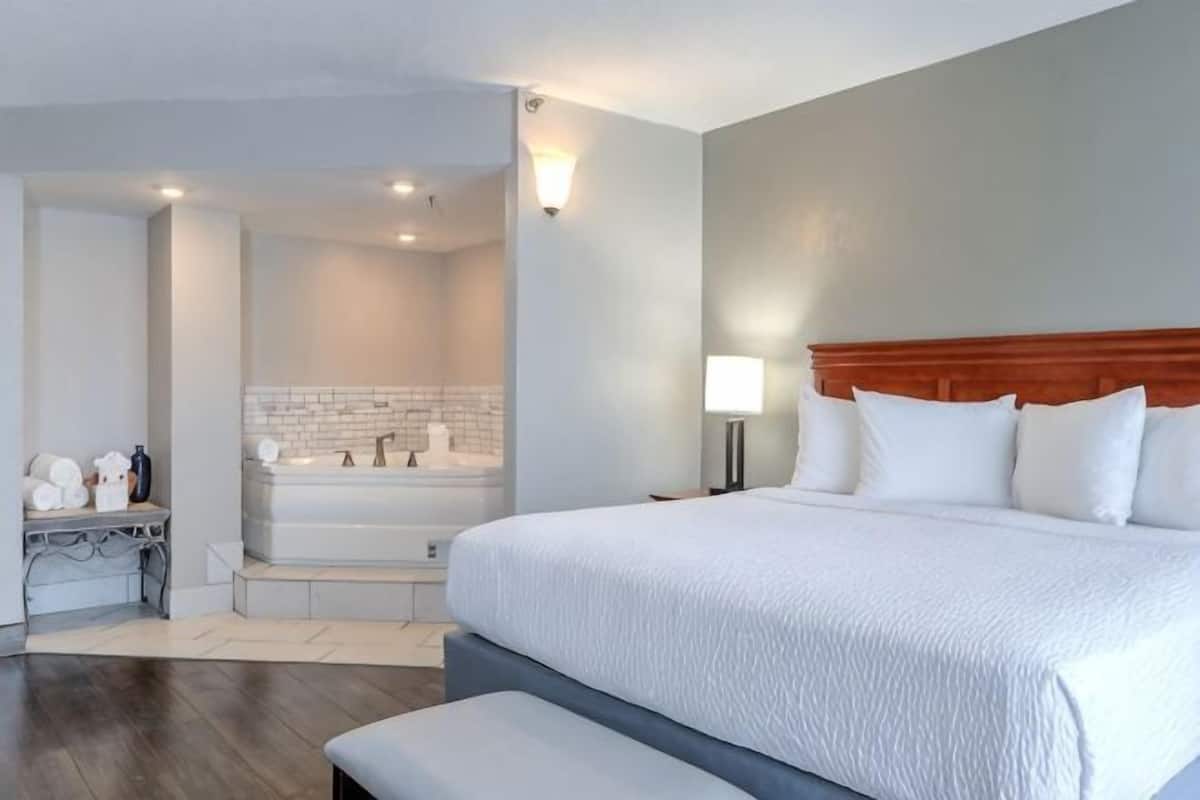 Habitación de hotel con una cama grande, baño privado con bañera y una pequeña zona de estar.