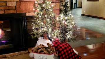 Un árbol de Navidad decorado en un vestíbulo con chimenea, una cesta de leños y un cojín a cuadros.