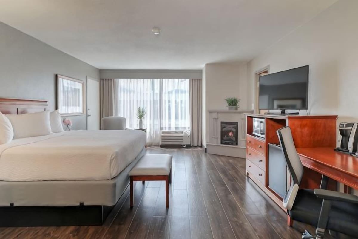 A hotel room with a bed, a desk, a chair, a television, and a fireplace.