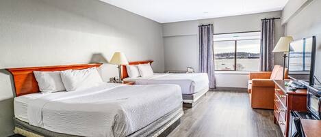 A hotel room with two beds, a television, a desk, and a view of the water.