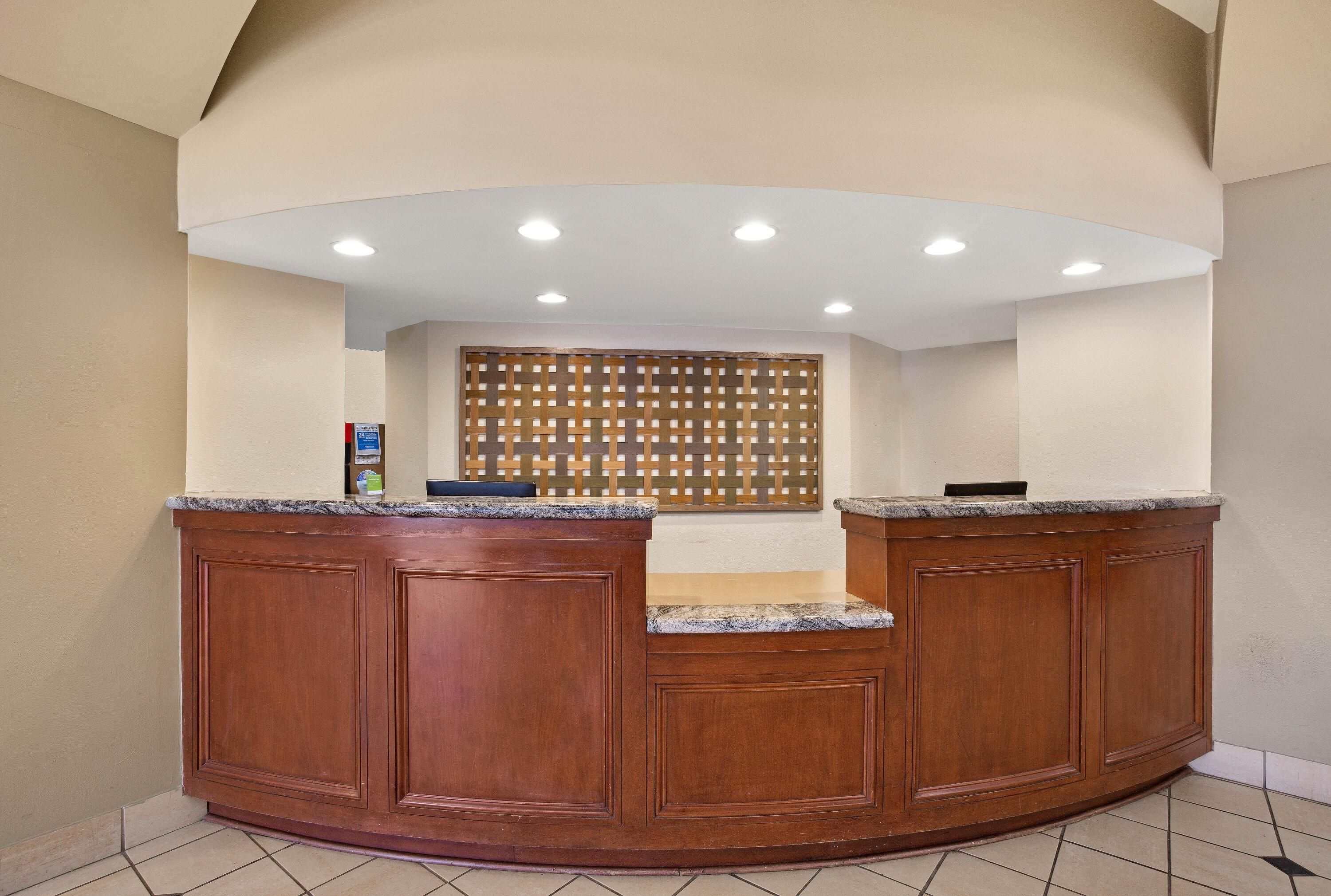 A reception desk with a wooden finish, a tiled floor, and a ceiling with recessed lighting.