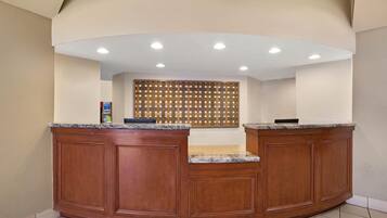 A reception desk with a wooden finish, a tiled floor, and a ceiling with recessed lighting.