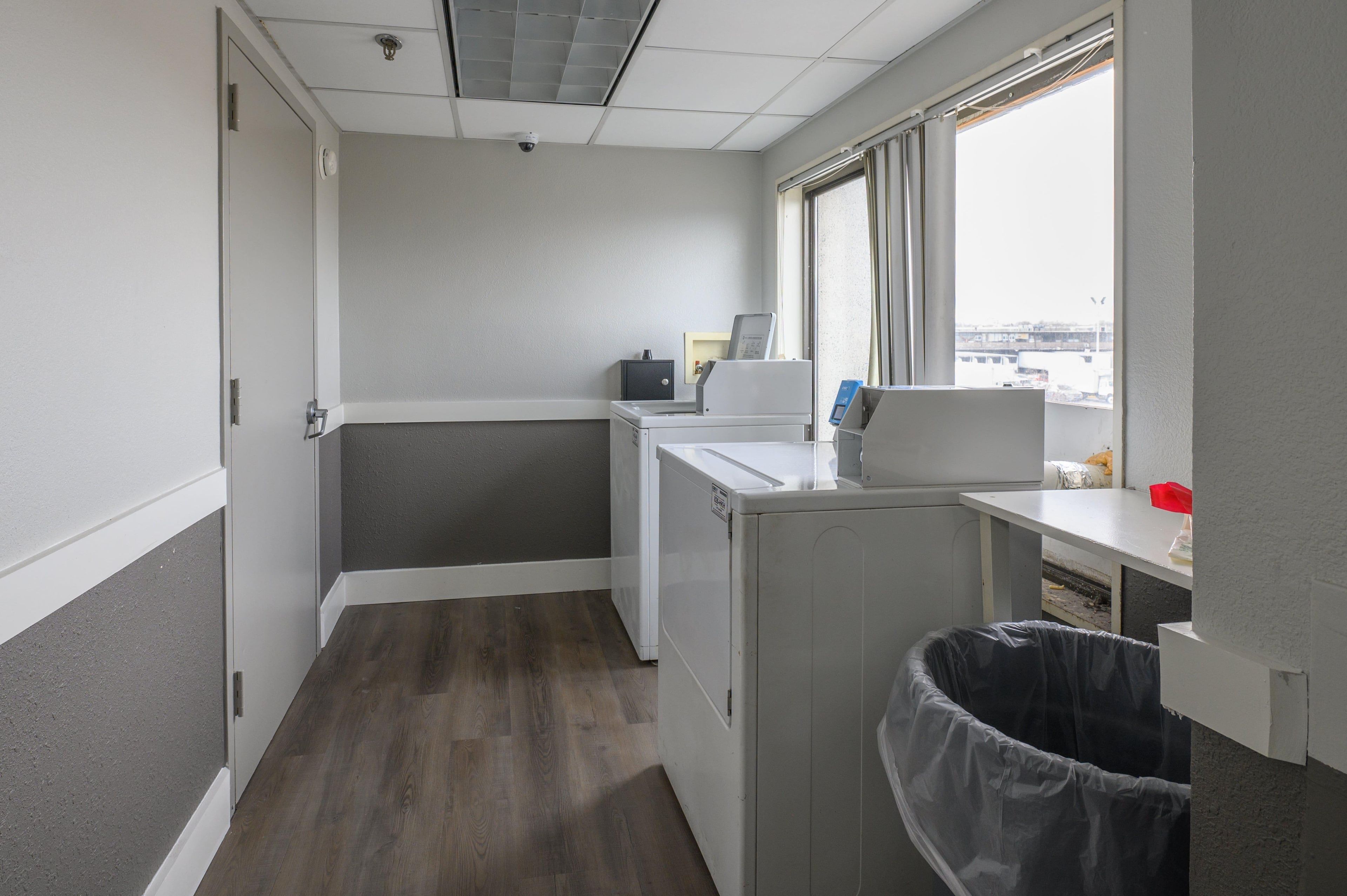 A compact laundry room with a washing machine, dryer, and a trash bin.