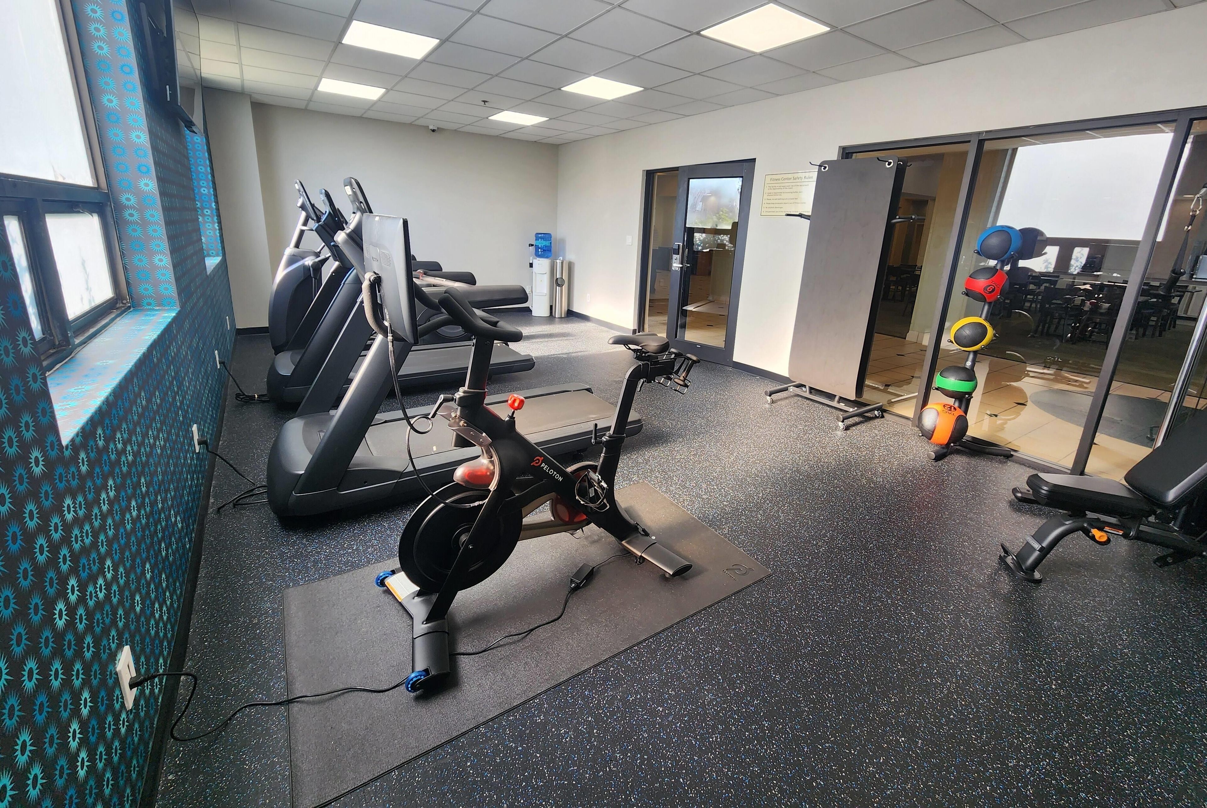 A fitness center with cardio equipment, a water dispenser, and a glass door leading to an outdoor area.