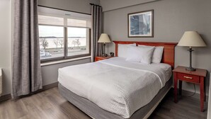Een hotelkamer met een groot bed, twee nachtkastjes met lampen, een raam met uitzicht en een fotokader aan de muur.