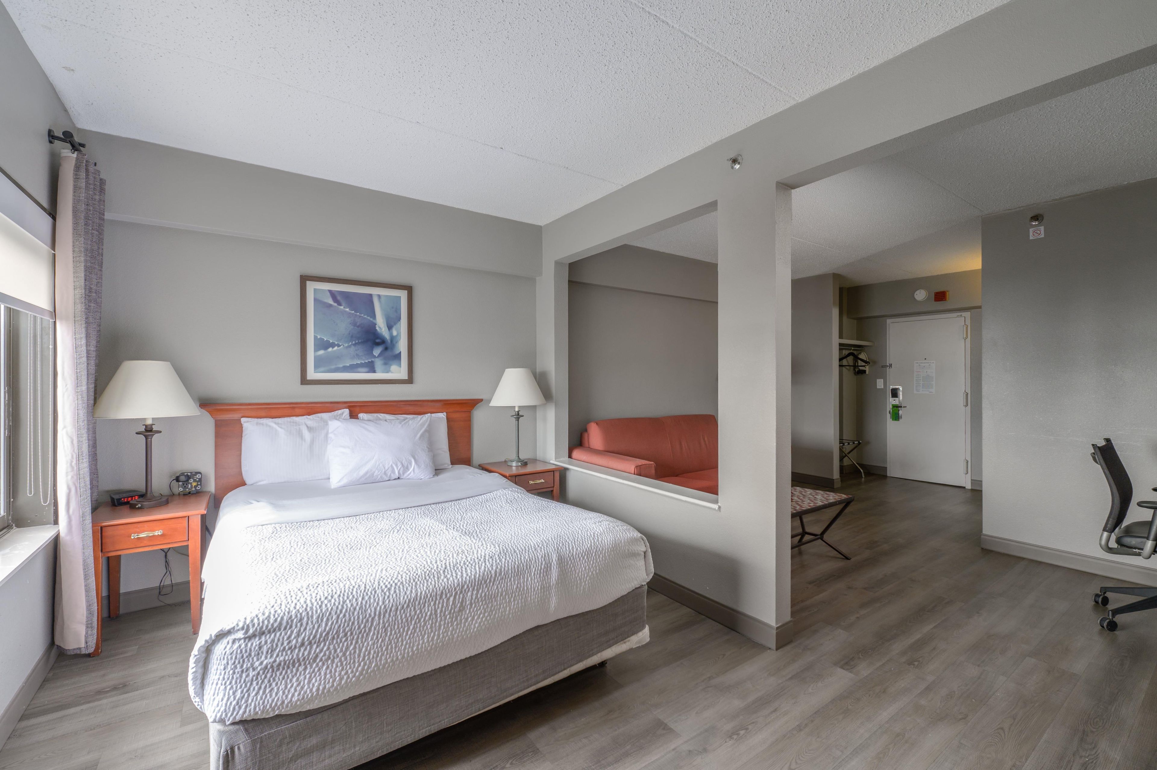 Une chambre d’hôtel comprenant un lit, deux tables de chevet, un bureau, une chaise et donnant sur le couloir.