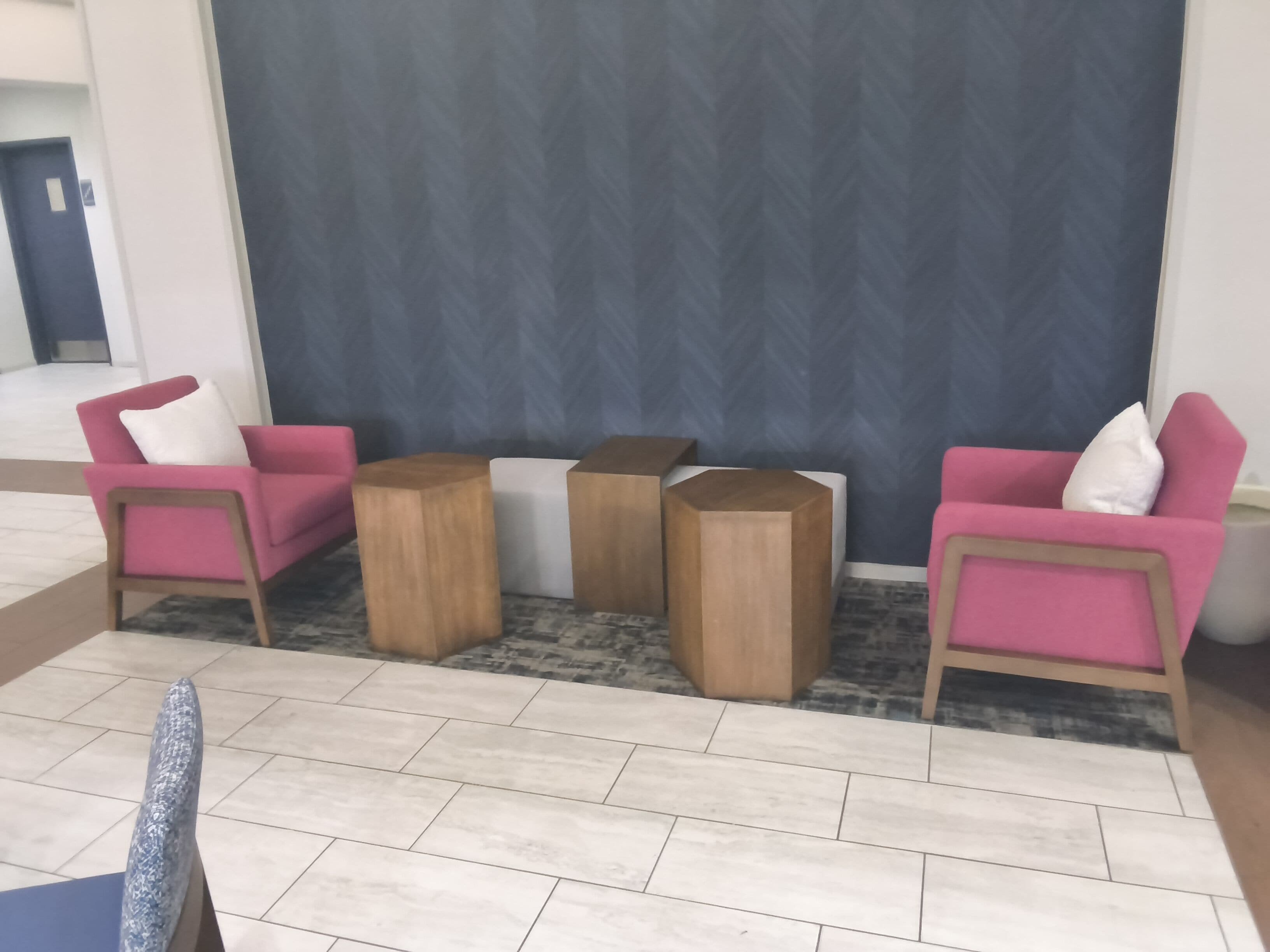 A modern lobby with a seating area featuring pink chairs and wooden side tables.