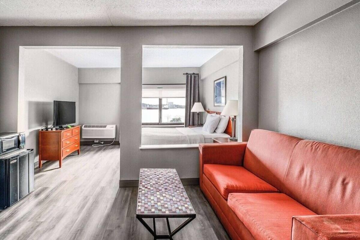A modern hotel room with a sofa, a TV, a dresser, and a window with a city view.