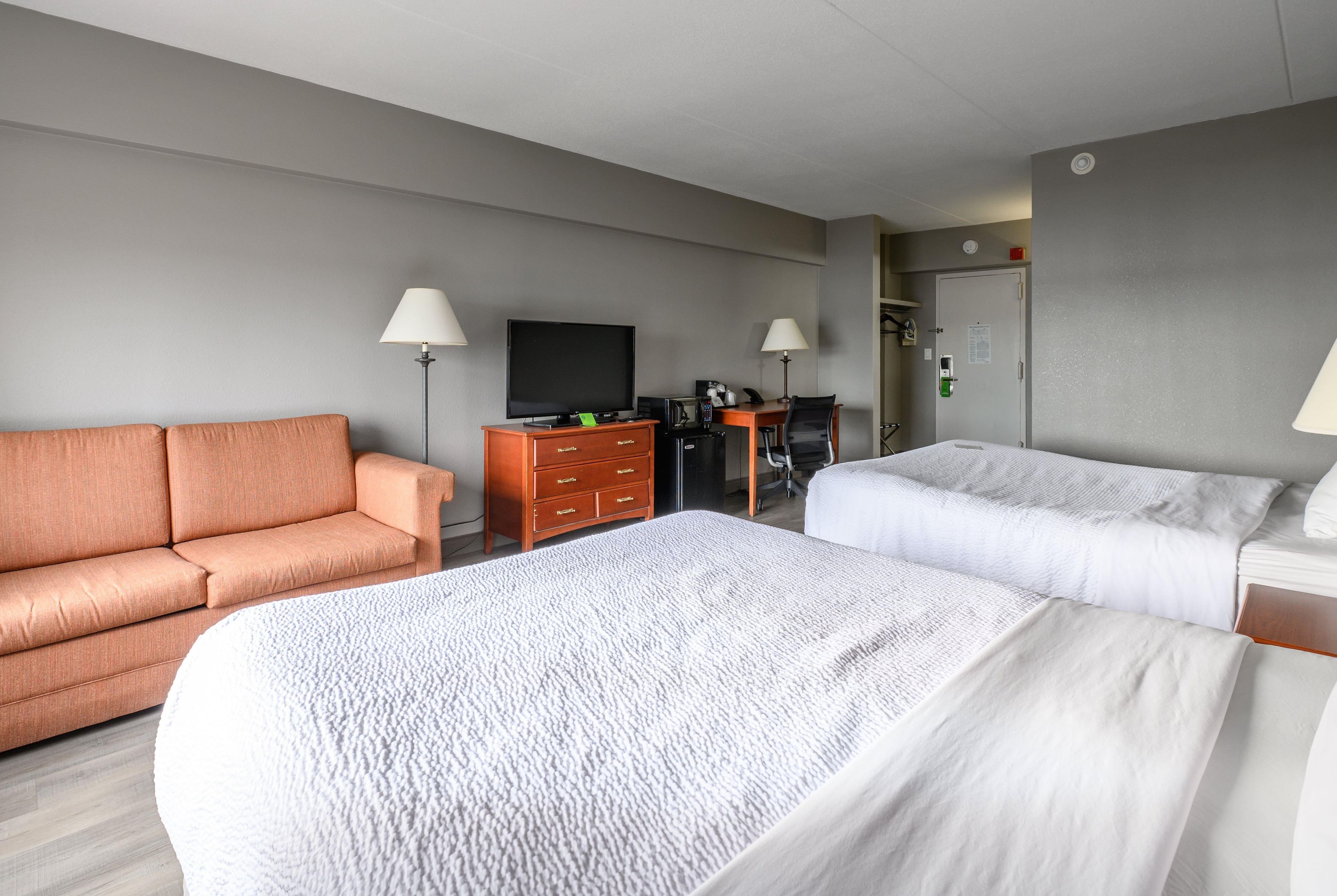 Habitación de hotel con sofá, escritorio con computadora, televisión y dos camas.