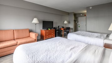 Habitación de hotel con sofá, escritorio con computadora, televisión y dos camas.