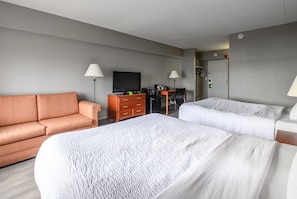 Een hotelkamer met een bank, een bureau met een computer, een televisie en twee bedden.