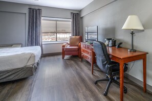 Une chambre d’hôtel avec un lit, un bureau avec une lampe, une chaise, une commode et une fenêtre donnant sur la ville.