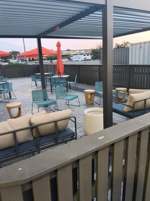 An outdoor seating area with tables and chairs, a covered section with a roof, and a view of the street with parked cars and a building in the background. - La Quinta Inn & Suites by Wyndham New Haven (New Haven)