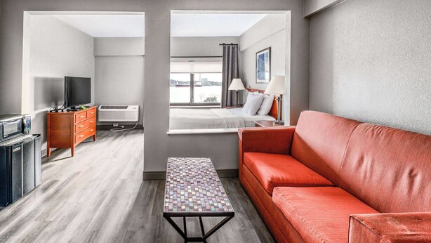 Een moderne hotelkamer met een rode bank, een kleine tafel, een televisie, een dressoir en een raam met uitzicht over de stad.