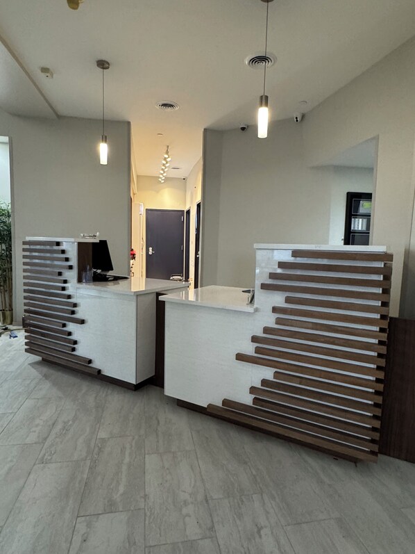 A reception area with two reception desks, a flat-screen TV, and a modern light fixture. - La Quinta Inn & Suites by Wyndham New Haven (New Haven)