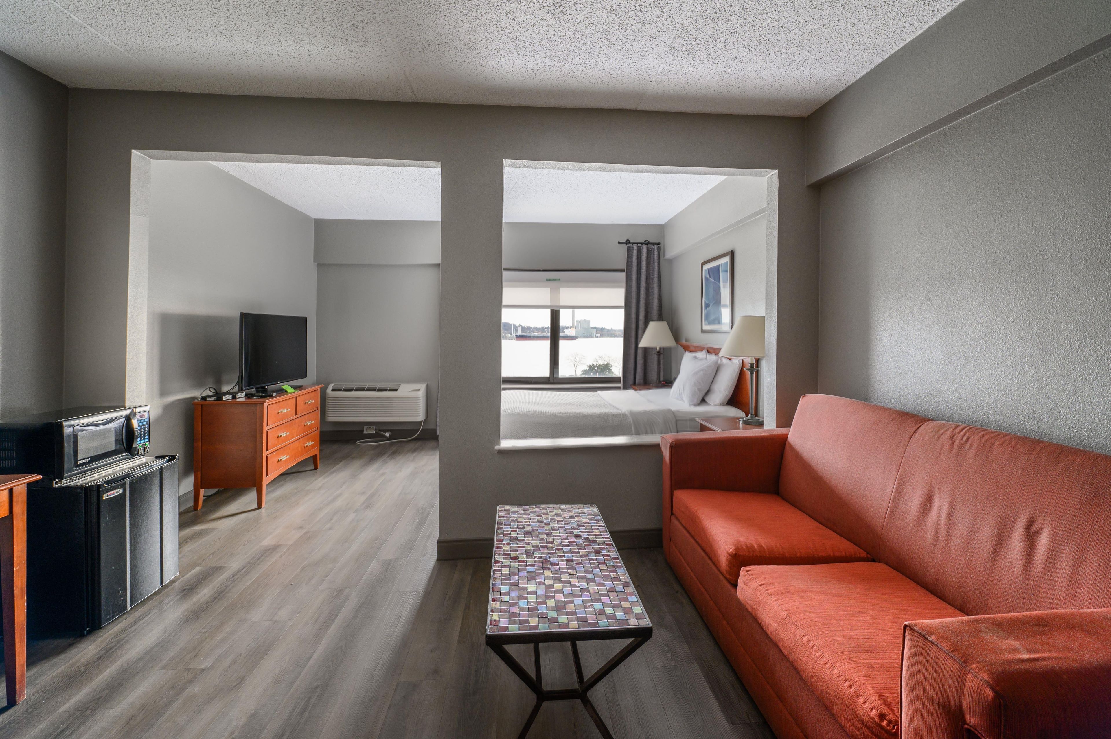 A hotel room with a sofa, a small table, a television, a dresser, and a window with a view.