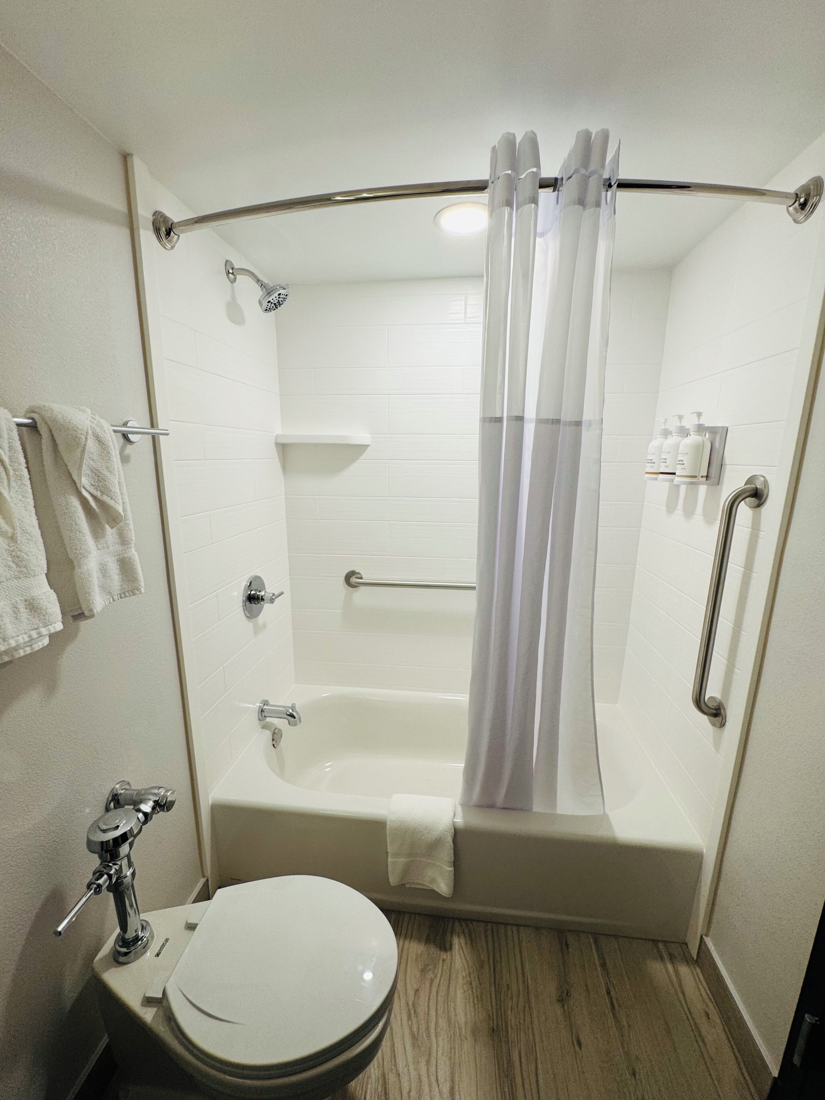 A bathroom with a bathtub, toilet, shower, and handrails.