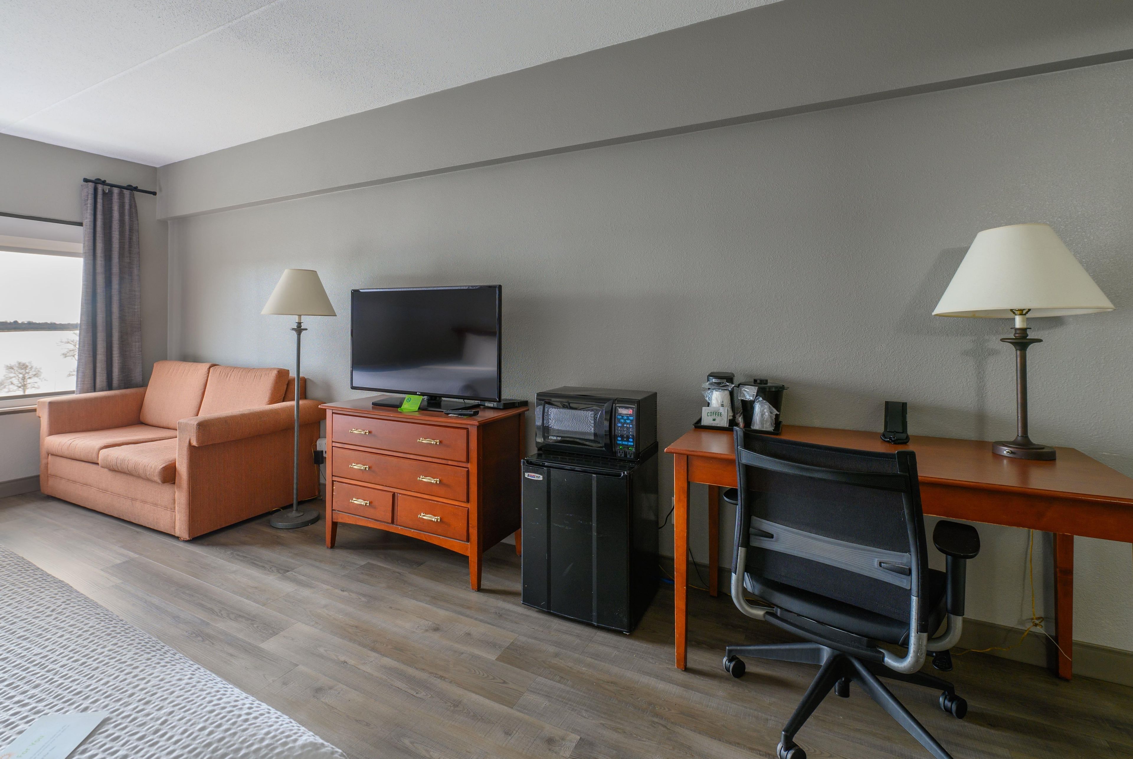 Habitación de hotel con sofá, escritorio con computadora, televisor, cafetera y una silla.