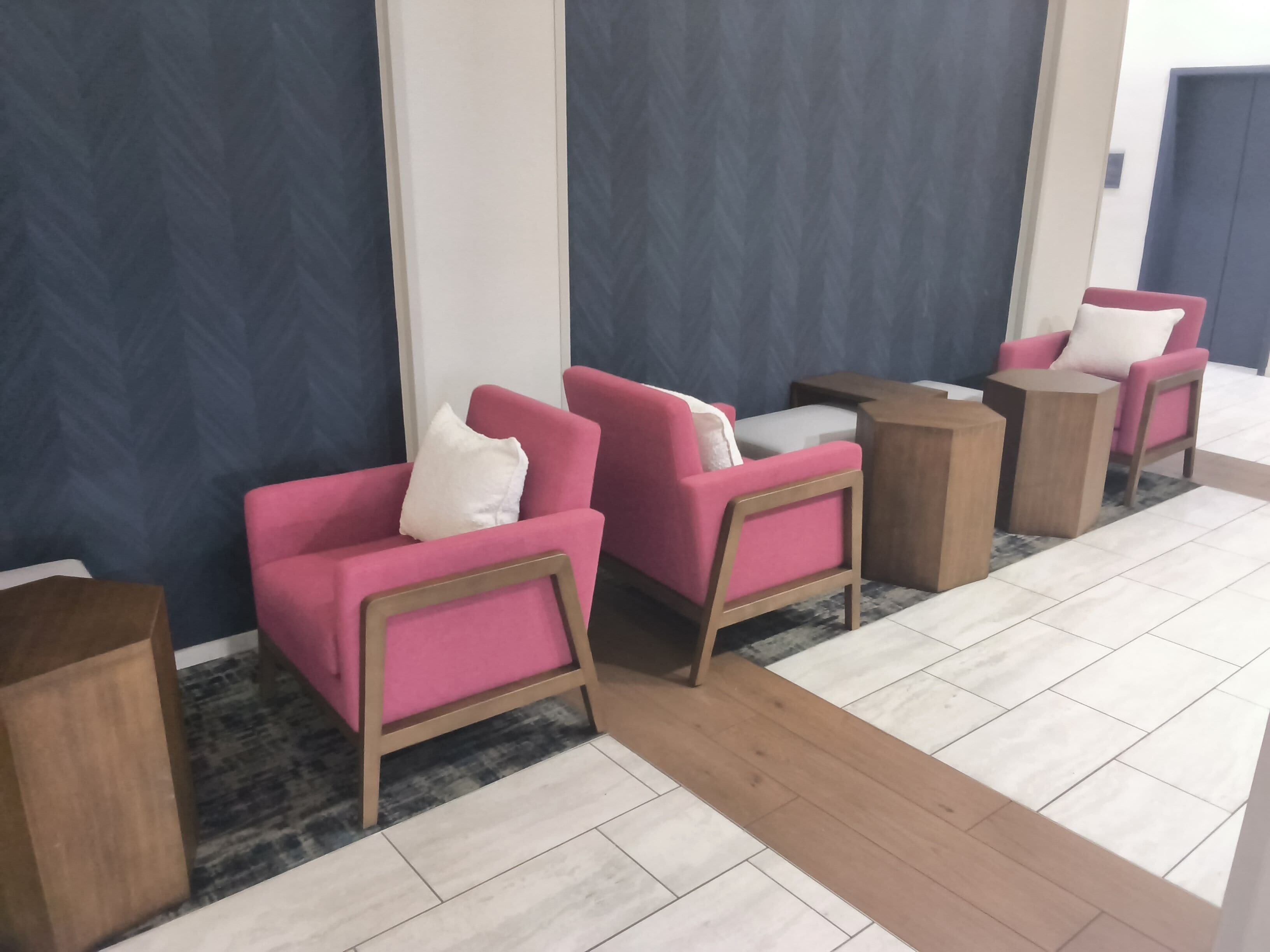 A seating area with two pink chairs and a small table, a wooden side table, and a patterned rug.