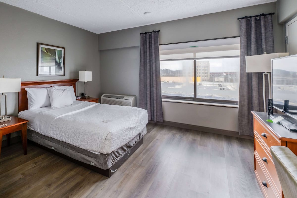 A hotel room with a large bed, a desk with a lamp, a dresser, and a window with curtains.
