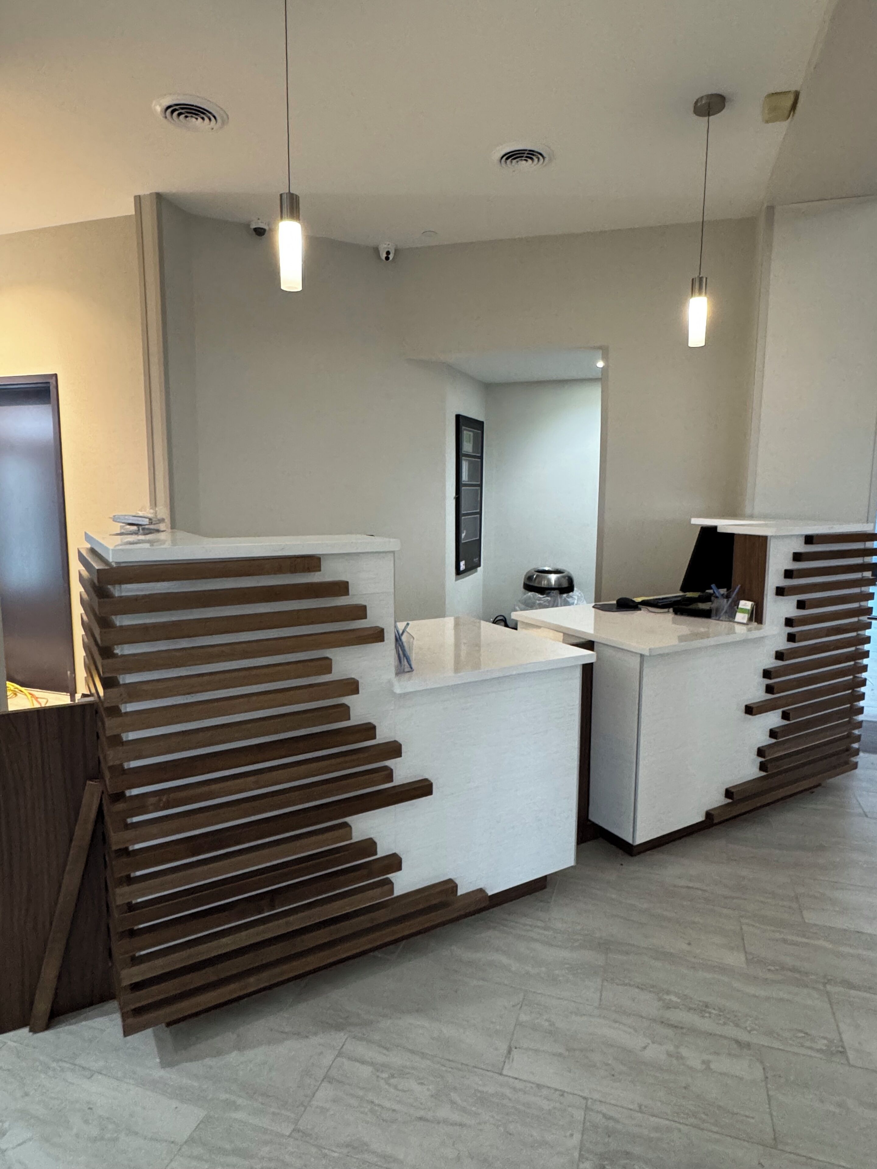 En receptionsdisk med modern design, med en vit yta och träribbor. Ovanför disken hänger två hänglampor, och en spegel syns i bakgrunden.
