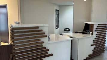 Una recepción con diseño moderno, que presenta una superficie blanca y tiras de madera. Dos lámparas colgantes iluminan el mostrador, y se ve un espejo al fondo.