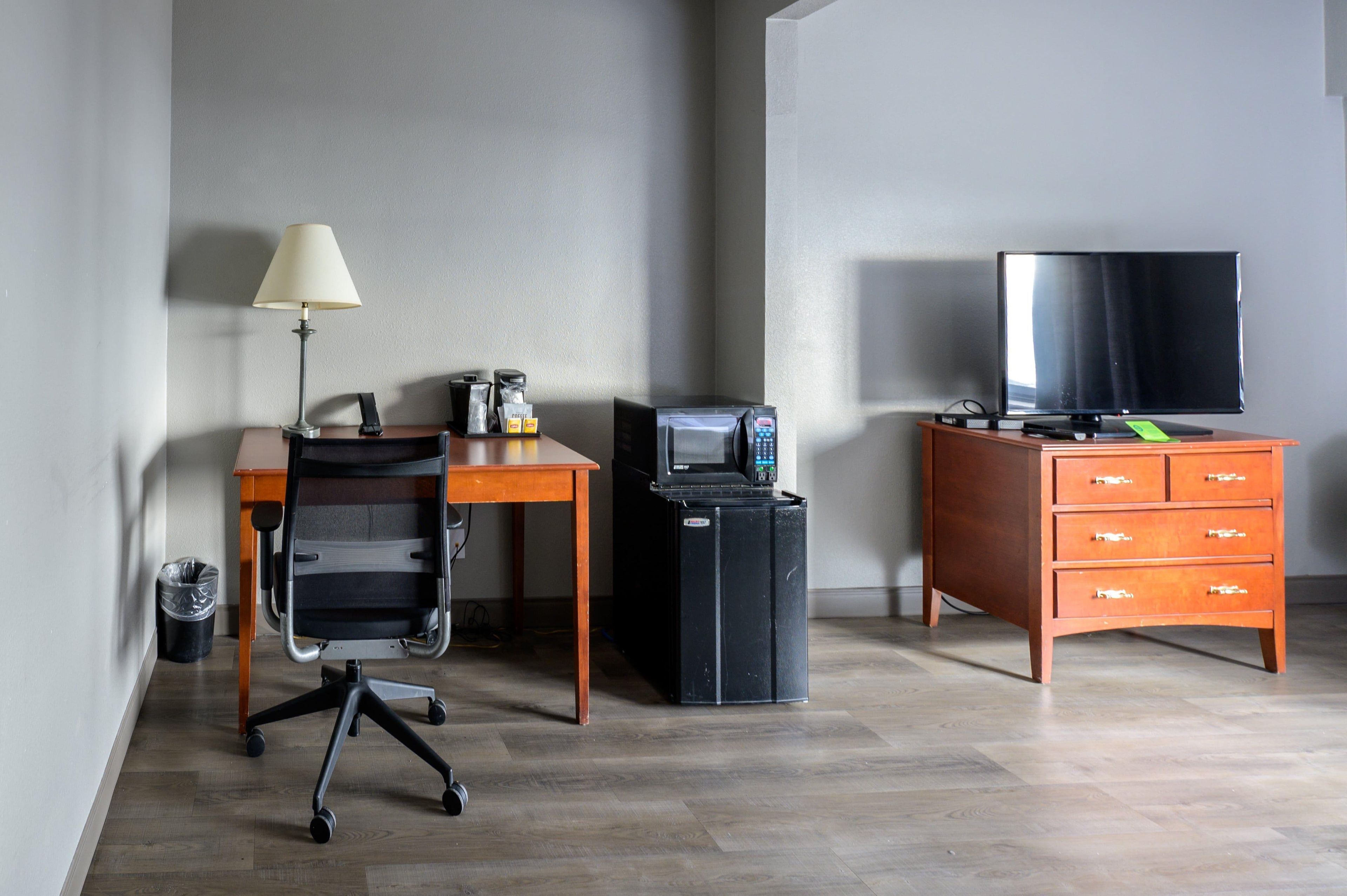 A hotel room with a desk, chair, television, and a small cabinet.