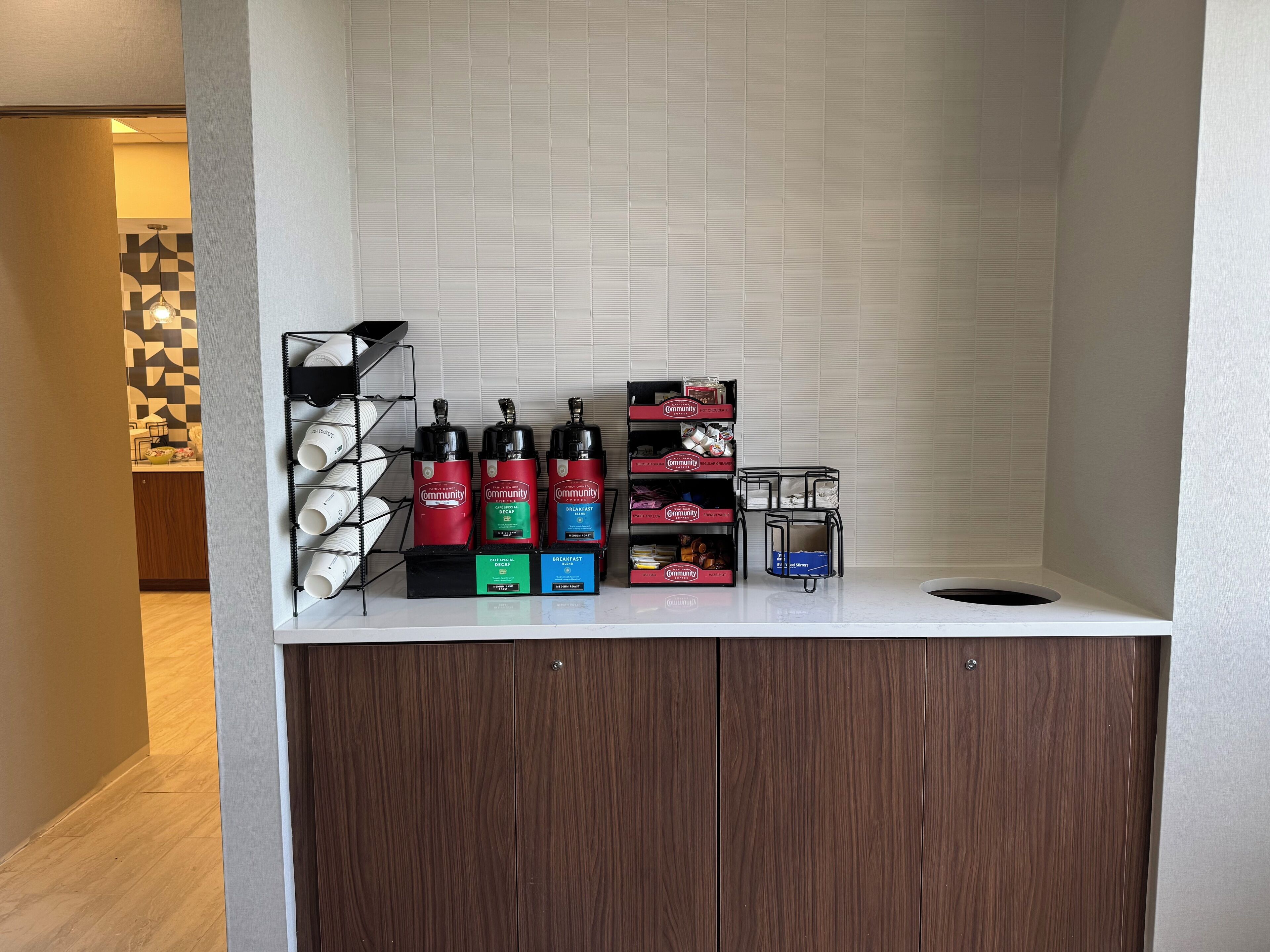 Un área de kitchenette con espacio para café, que incluye dispensadores y una cafetera, además de un pequeño cubo de basura.