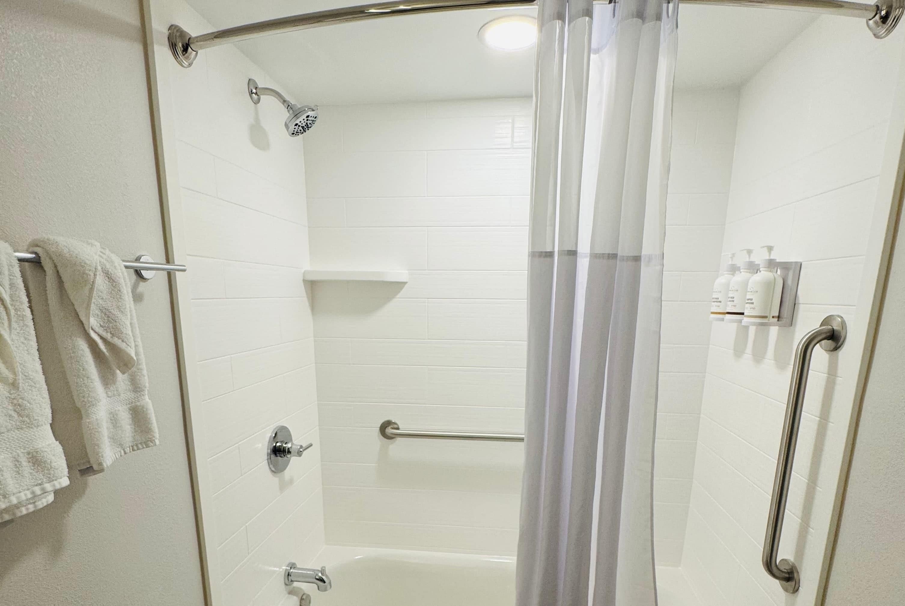 A shower with a glass door, a handheld showerhead, a grab bar, and a towel rack with towels.