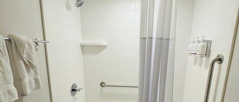 Une douche avec une porte en verre, un pommeau de douche amovible, une barre d’appui et un porte-serviettes avec des serviettes.