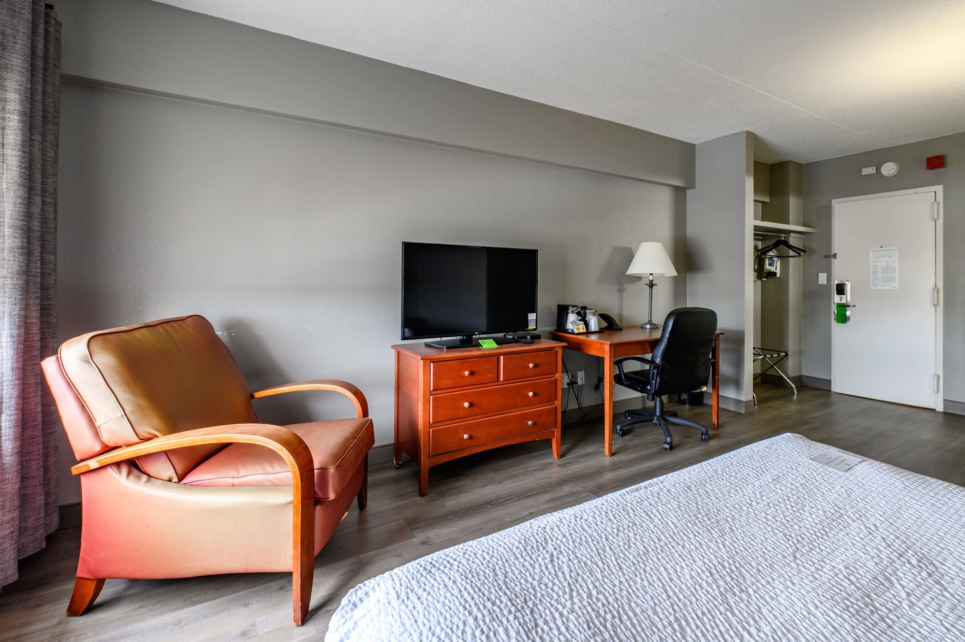 Habitación de hotel con cama, escritorio con televisor, silla y cómoda.