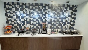 Een buffetopstelling met een wand met geometrisch patroon, een fruitpresentatie en diverse gerechten.
