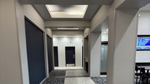 Een hotelgangen met een betegelde vloer, een deur in het midden en een zithoek met stoelen en een tafel.