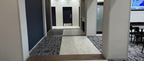 Un pasillo de hotel con suelo de baldosas, una puerta central y una zona de estar con sillas y una mesa.