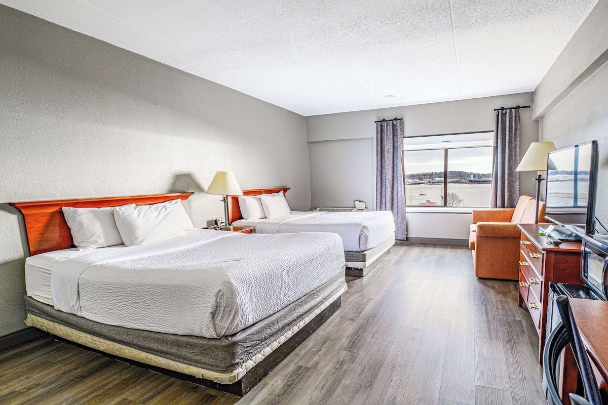 A hotel room with two beds, a sofa, a TV, and a view of the city.