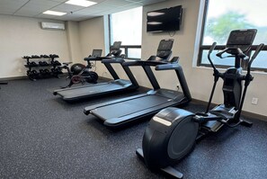 Een sportschool met loopbanden, een elliptische trainer en een dumbbellsysteem.