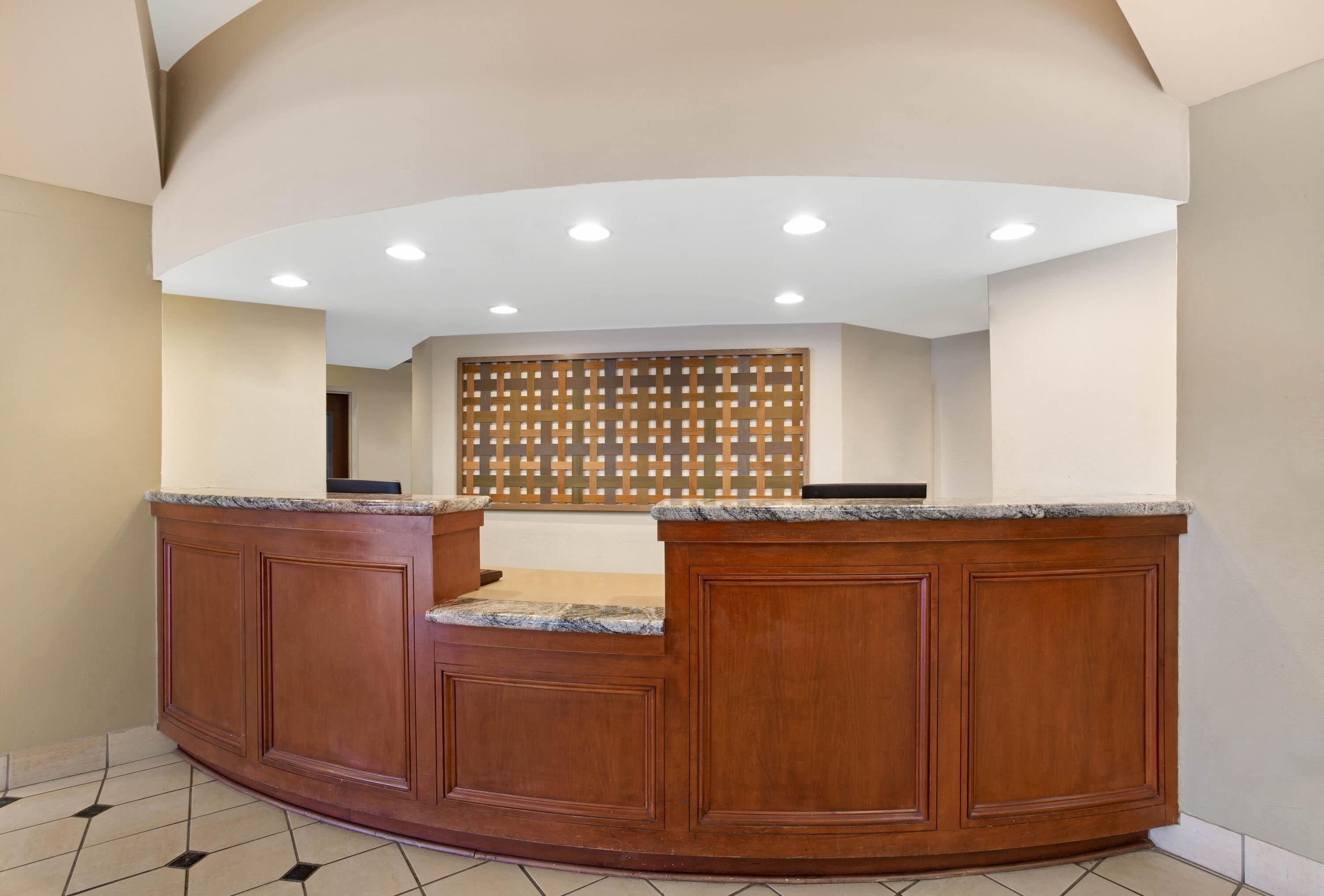 A reception area with a wooden reception desk, a tiled floor, and a ceiling with recessed lighting.