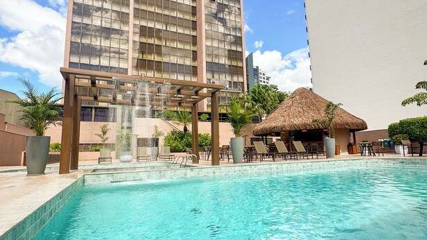 A hotel with a large pool, a waterfall feature, and a thatched-roof structure. - Castro's Park Hotel (Goiania)