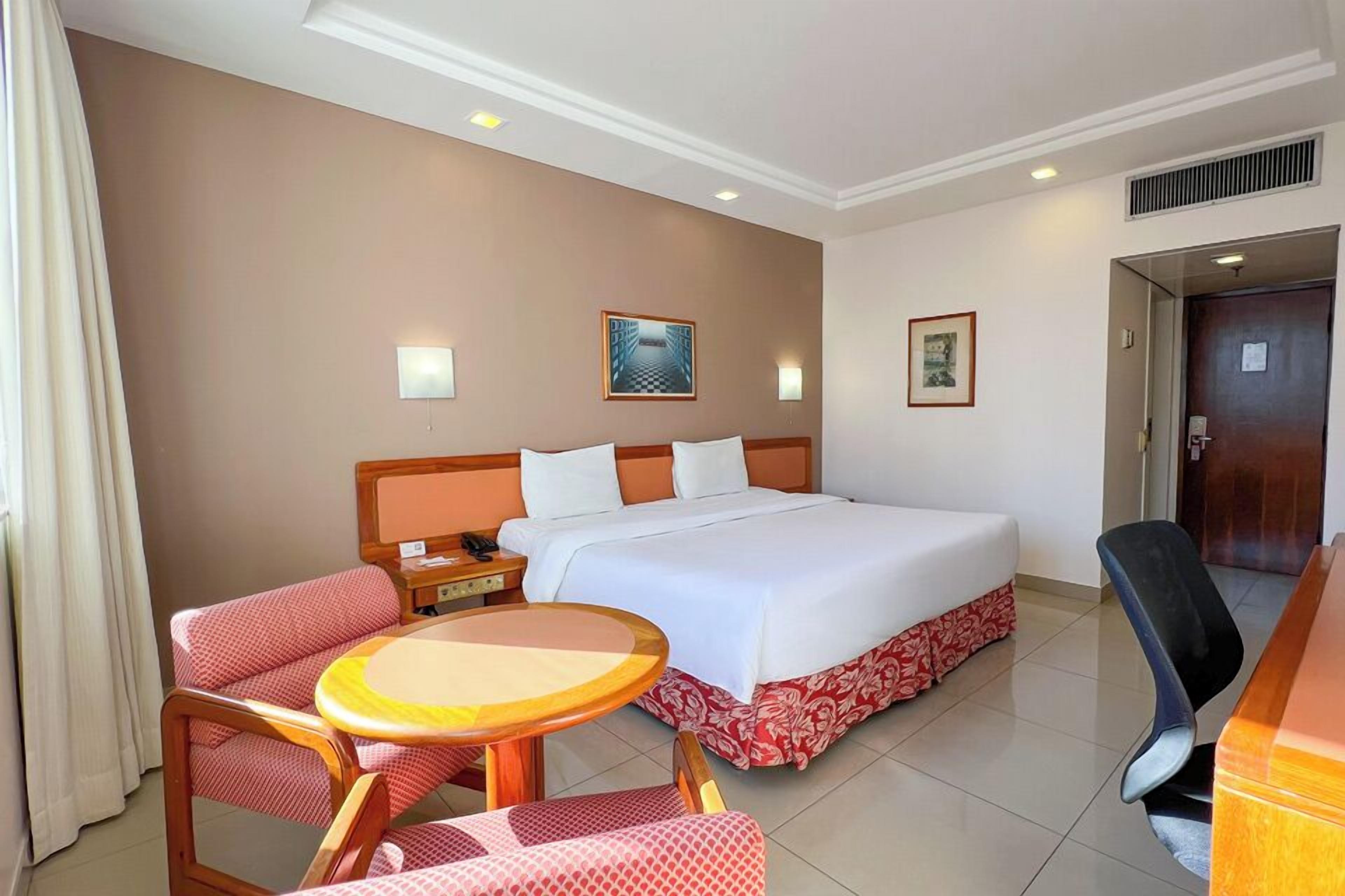 Habitación de hotel con una cama grande, una mesita de noche, una silla, una pequeña mesa redonda y un escritorio.