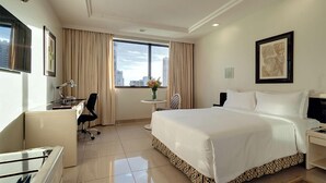 A hotel room with a large bed, a desk, a chair, a small table with a vase of flowers, and a city view through the window. - Castro's Park Hotel (Goiania)