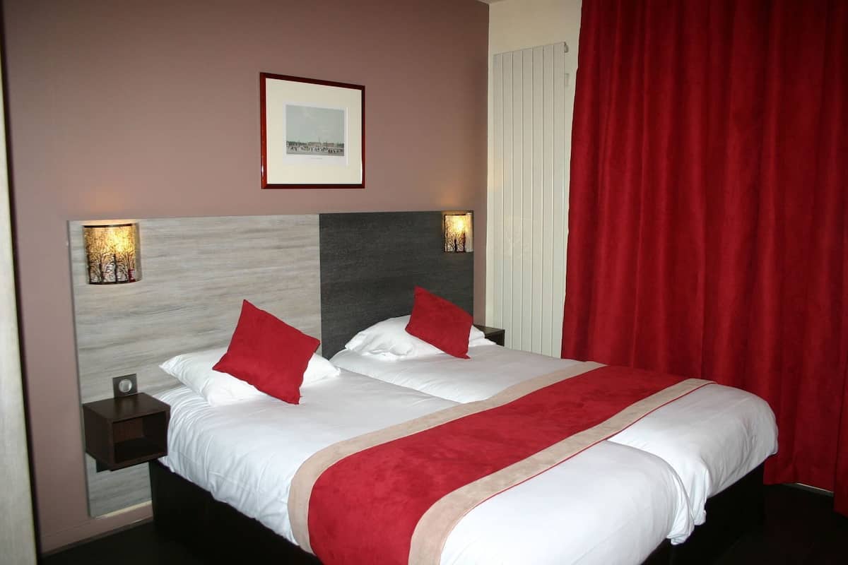 A hotel room with a bed, two nightstands, a framed picture on the wall, and a red curtain.